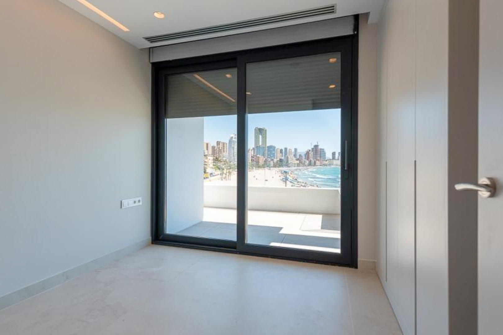 Bedroom featuring floor-to-ceiling wardrobes and a large sliding glass door opening onto a terrace with views of the Benidorm coastline.