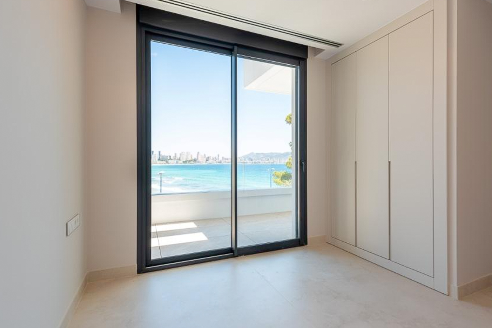 Bedroom with floor-to-ceiling fitted wardrobes and large sliding doors opening onto a terrace with views of the Mediterranean Sea and Benidorm.