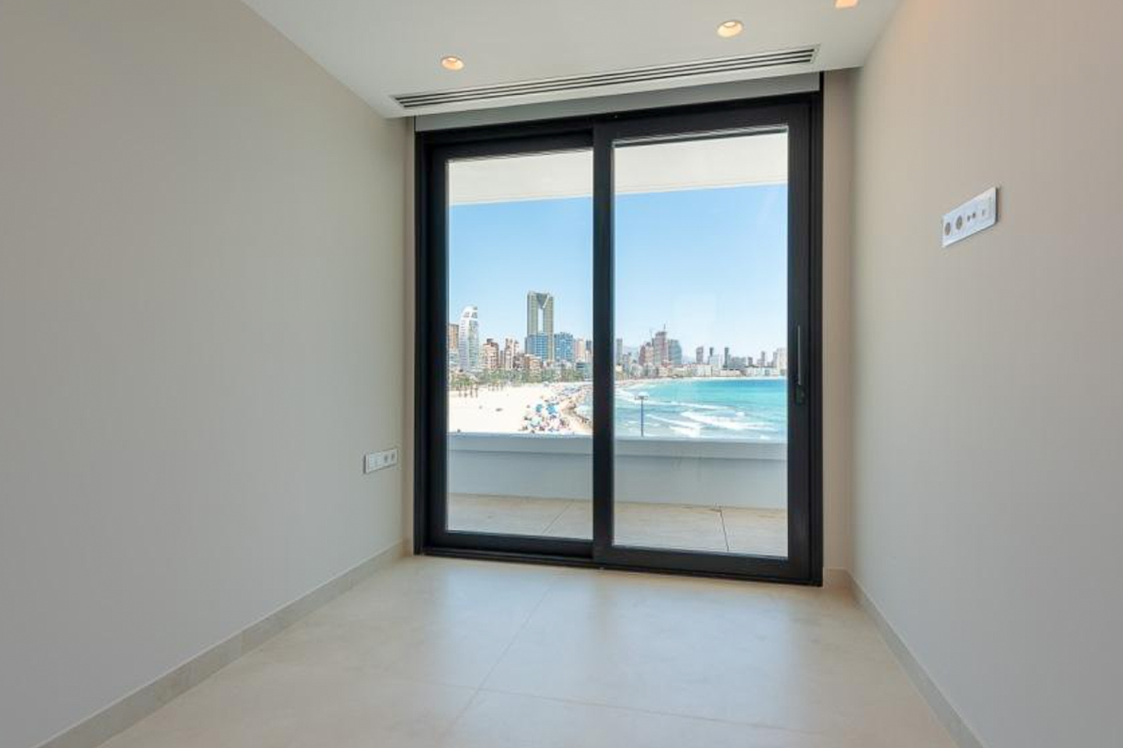Bright interior featuring light porcelain tiling and floor-to-ceiling sliding doors with direct views of the Benidorm coastline and skyline.