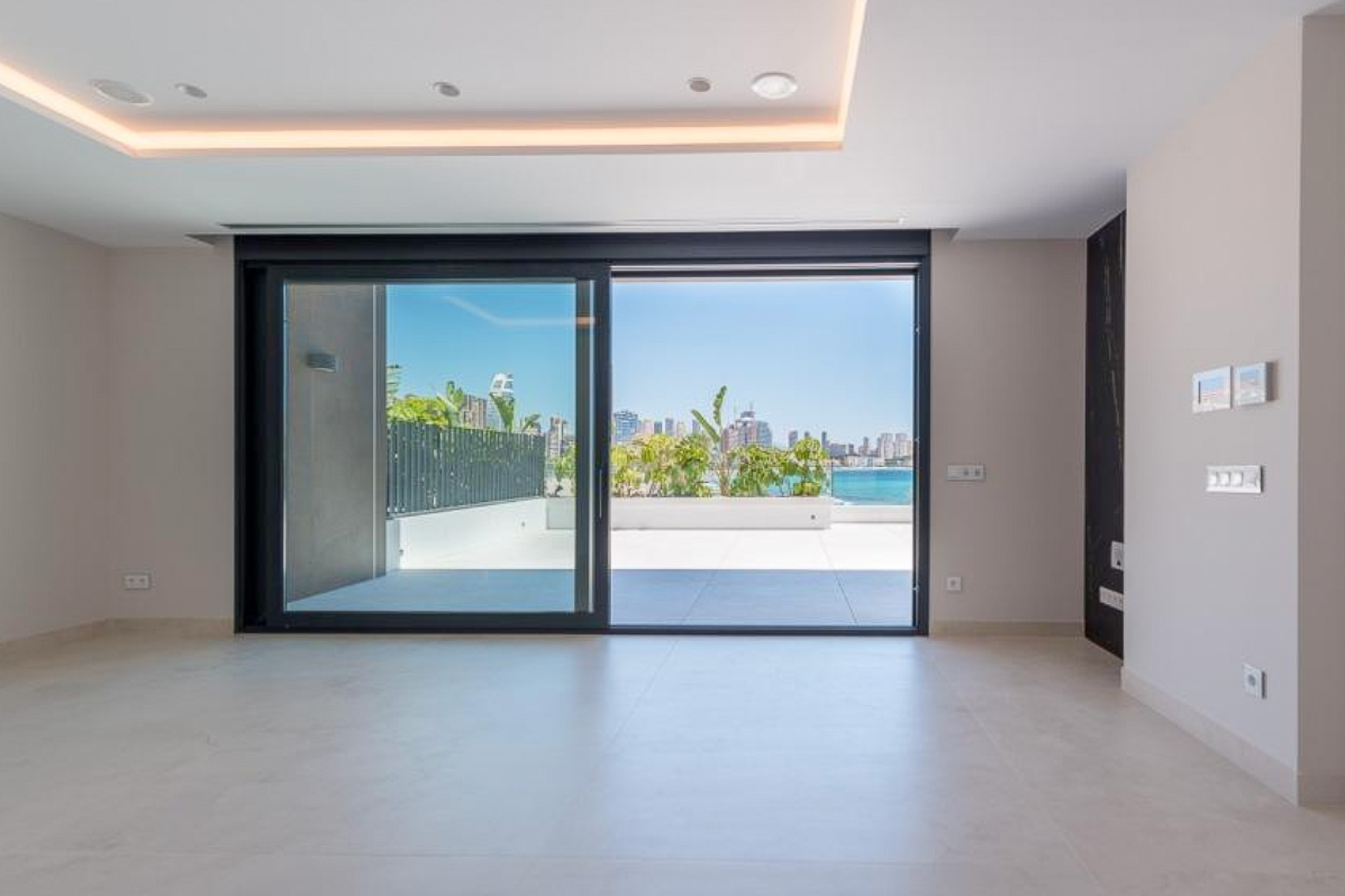 Bright living area featuring large-format ceramic flooring and sliding glass doors opening onto a private terrace with panoramic views of the Benidorm skyline.
