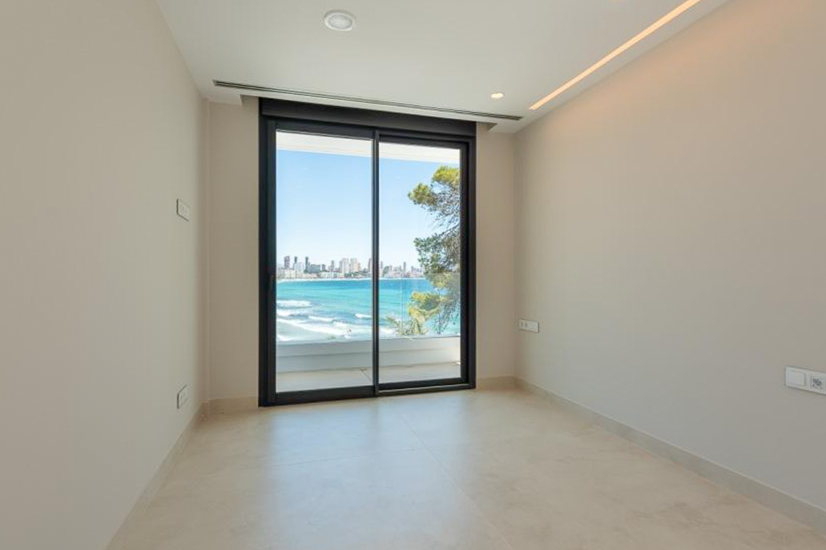 Bright room featuring porcelain flooring, recessed LED lighting, and large sliding doors opening to a terrace with panoramic Mediterranean views.