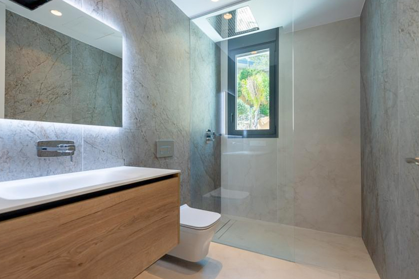 Designer bathroom featuring stone-effect wall tiles, a floating wooden vanity, backlit mirror, and a walk-in shower with a ceiling-mounted rainfall head.