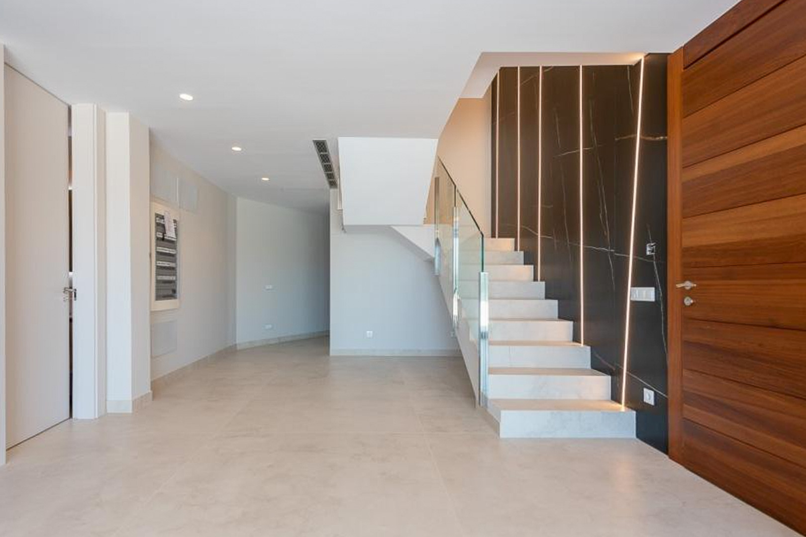 Entrance hall featuring a white stone staircase with glass railing and a dark marble-effect accent wall with vertical recessed LED lighting.
