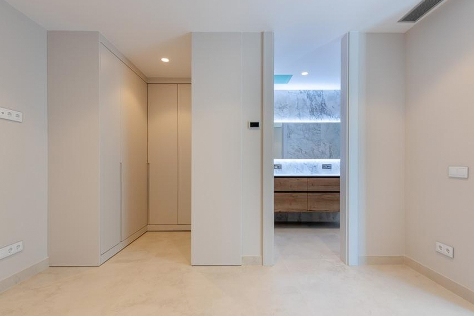 Master bedroom suite featuring floor-to-ceiling wardrobes and an ensuite bathroom with marble wall cladding, a wooden vanity, and recessed LED lighting.