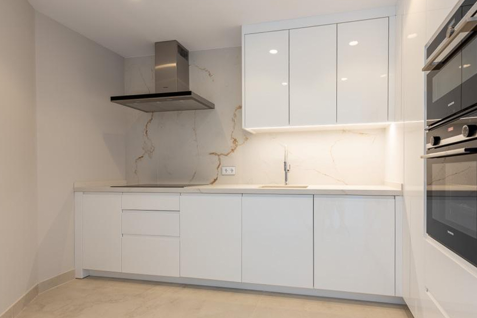 Minimalist designer kitchen featuring handleless white cabinetry, a marble-effect backsplash with gold veining, and integrated high-end appliances.