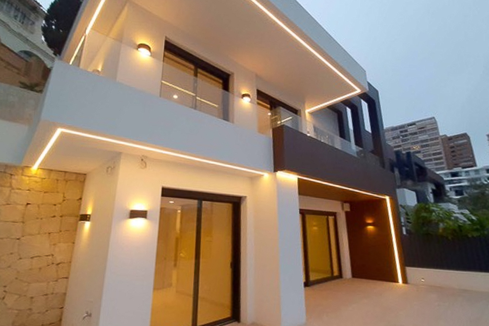 Modern exterior facade featuring integrated LED strip lighting, glass balcony railings, and large sliding glass doors in a minimalist architectural style.