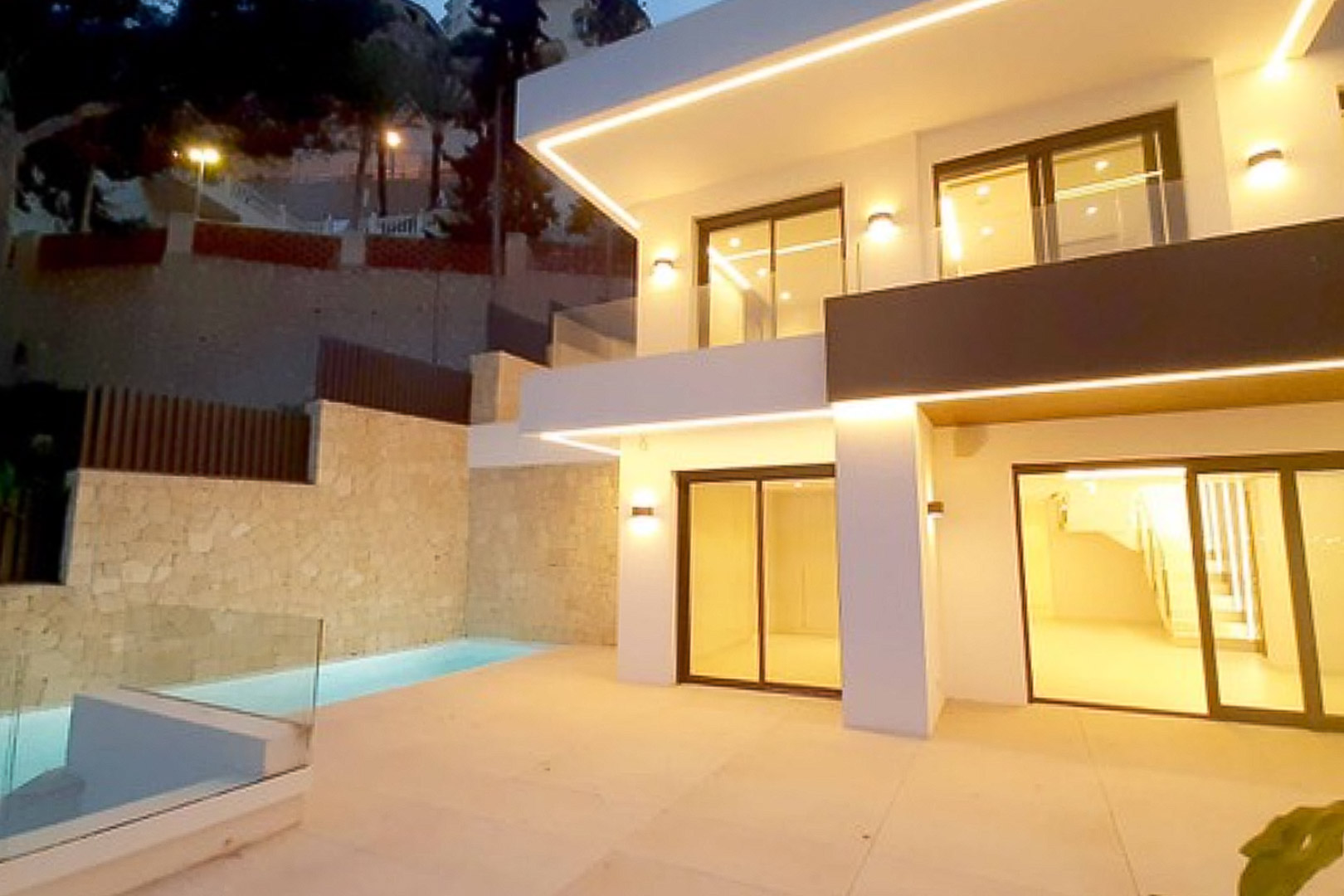Modern facade featuring integrated LED lighting, a porcelain tiled terrace, and a private pool set against natural stone walls.