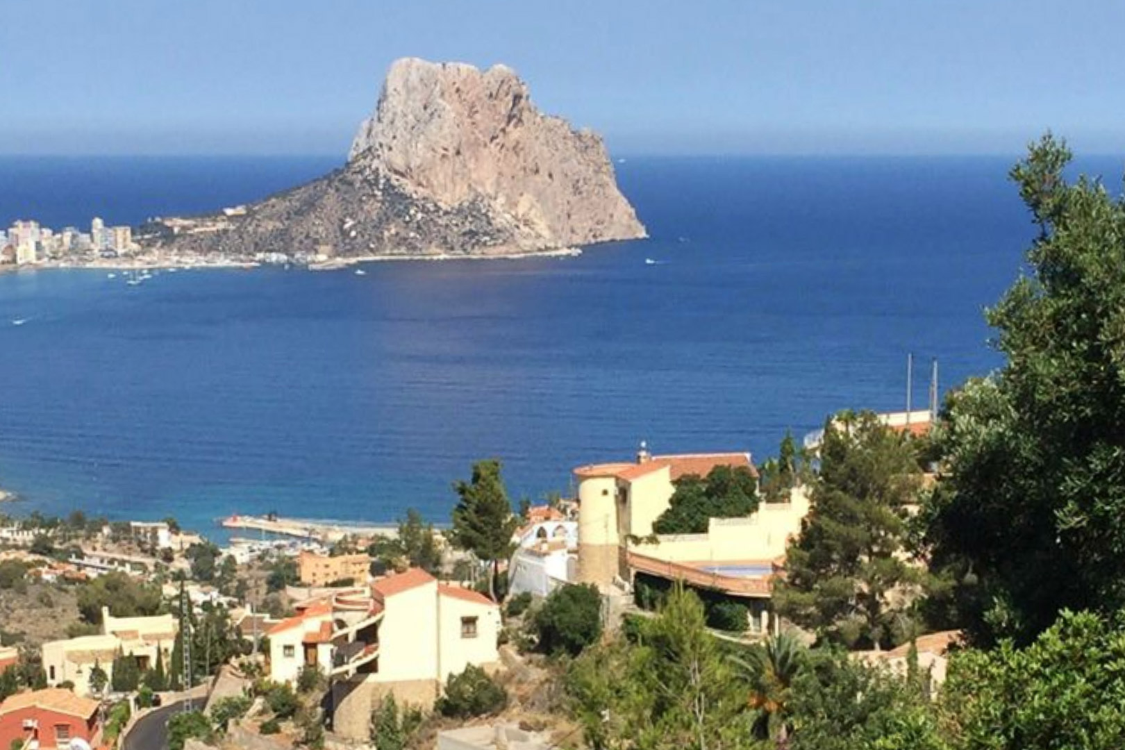 Elevated panoramic view of the Peñón de Ifach and the Mediterranean Sea, overlooking the residential landscape and lush greenery of Calpe.