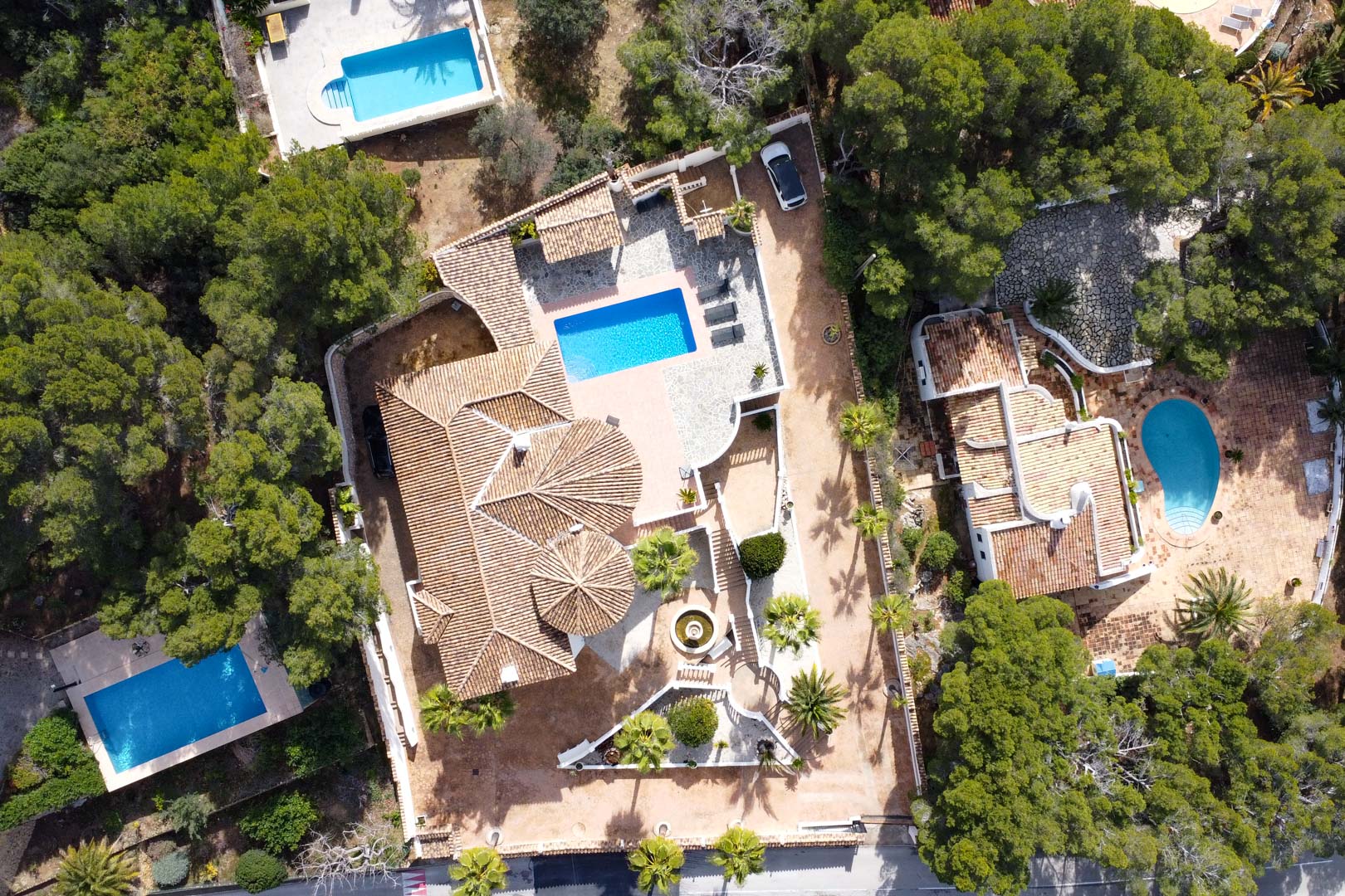 Aerial bird's-eye view of the villa featuring terracotta tiled roofs, a rectangular swimming pool, and stone-paved terraces set within a lush Mediterranean landscape.
