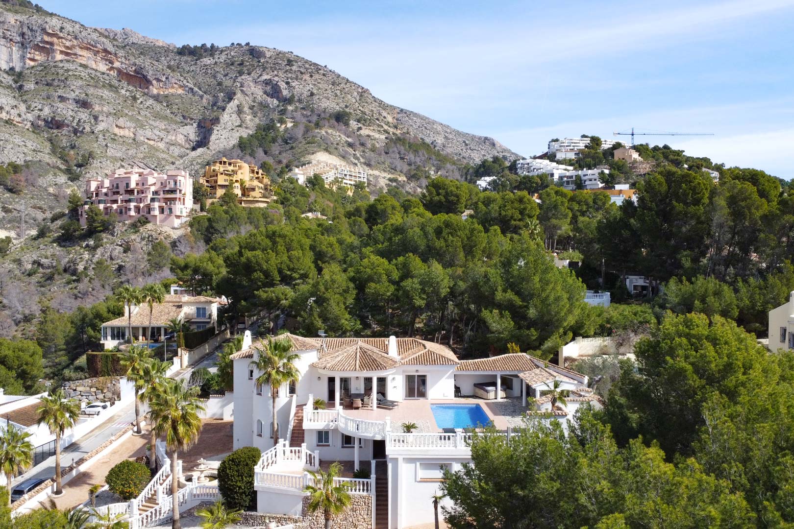 Aerial perspective of the villa showcasing terracotta roofs, a private swimming pool, and white terraces, set against the backdrop of the Sierra de Bernia.