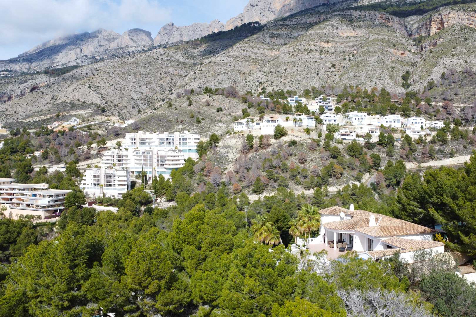 Aerial view of the Mediterranean villa with terracotta roofing, nestled among pine trees at the base of the Sierra de Bernia mountain range.