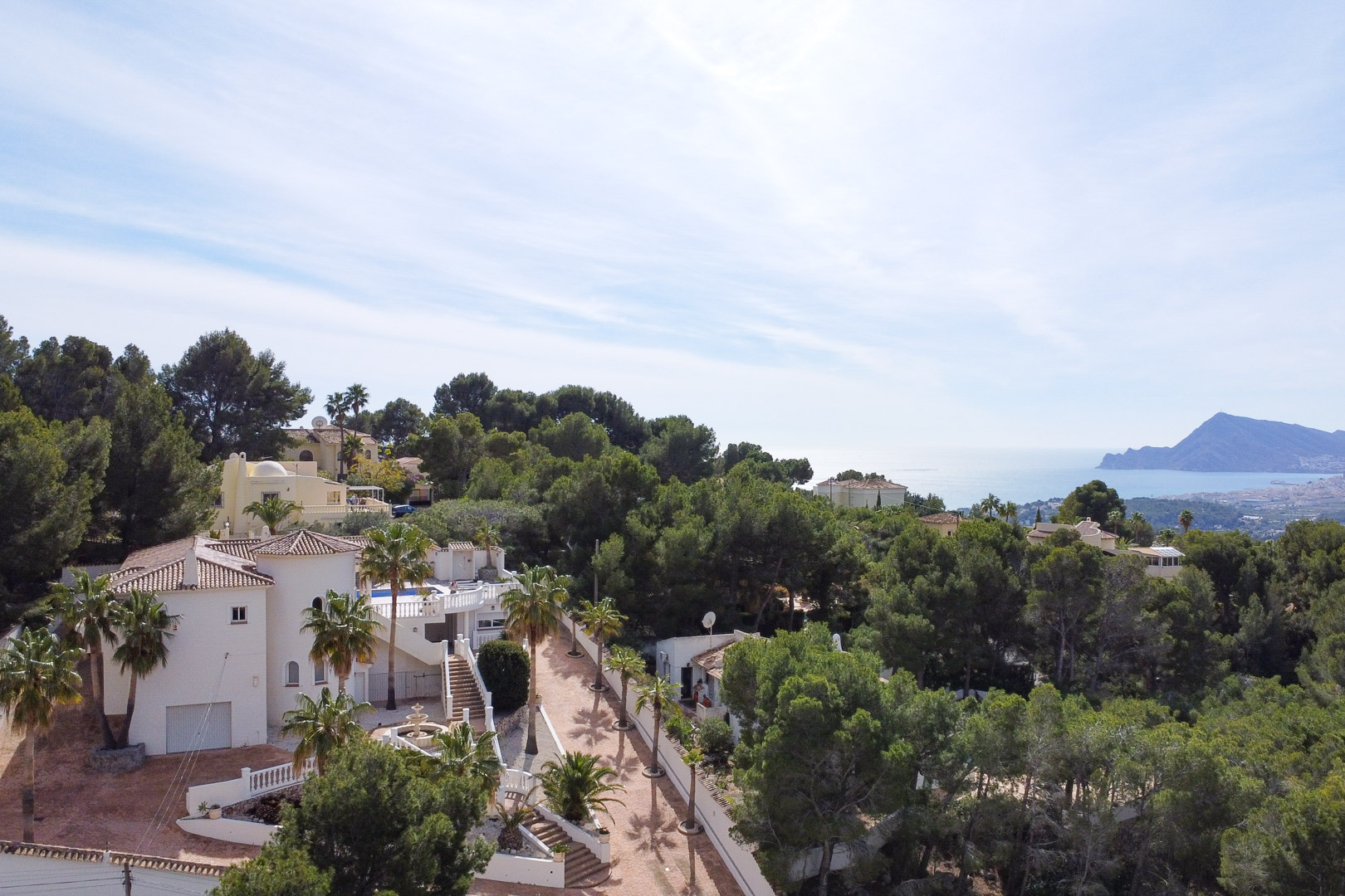 Aerial view of the white Mediterranean villa featuring a circular tower, terracotta roofs, and palm-lined grounds with views of the sea and coastline.