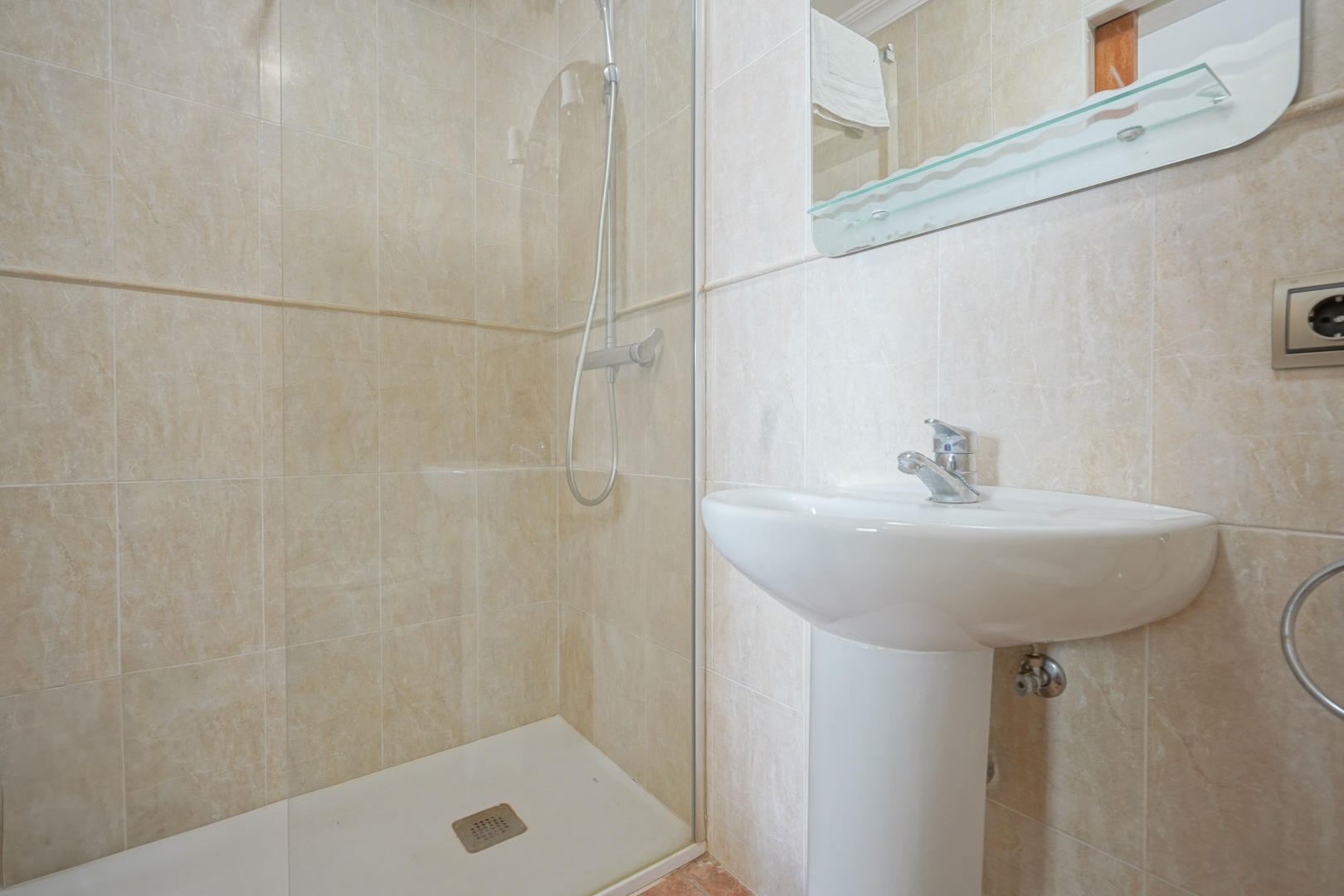 Bathroom featuring beige marble-effect tiling, a white pedestal sink, and a walk-in shower with a fixed glass partition and chrome fixtures.
