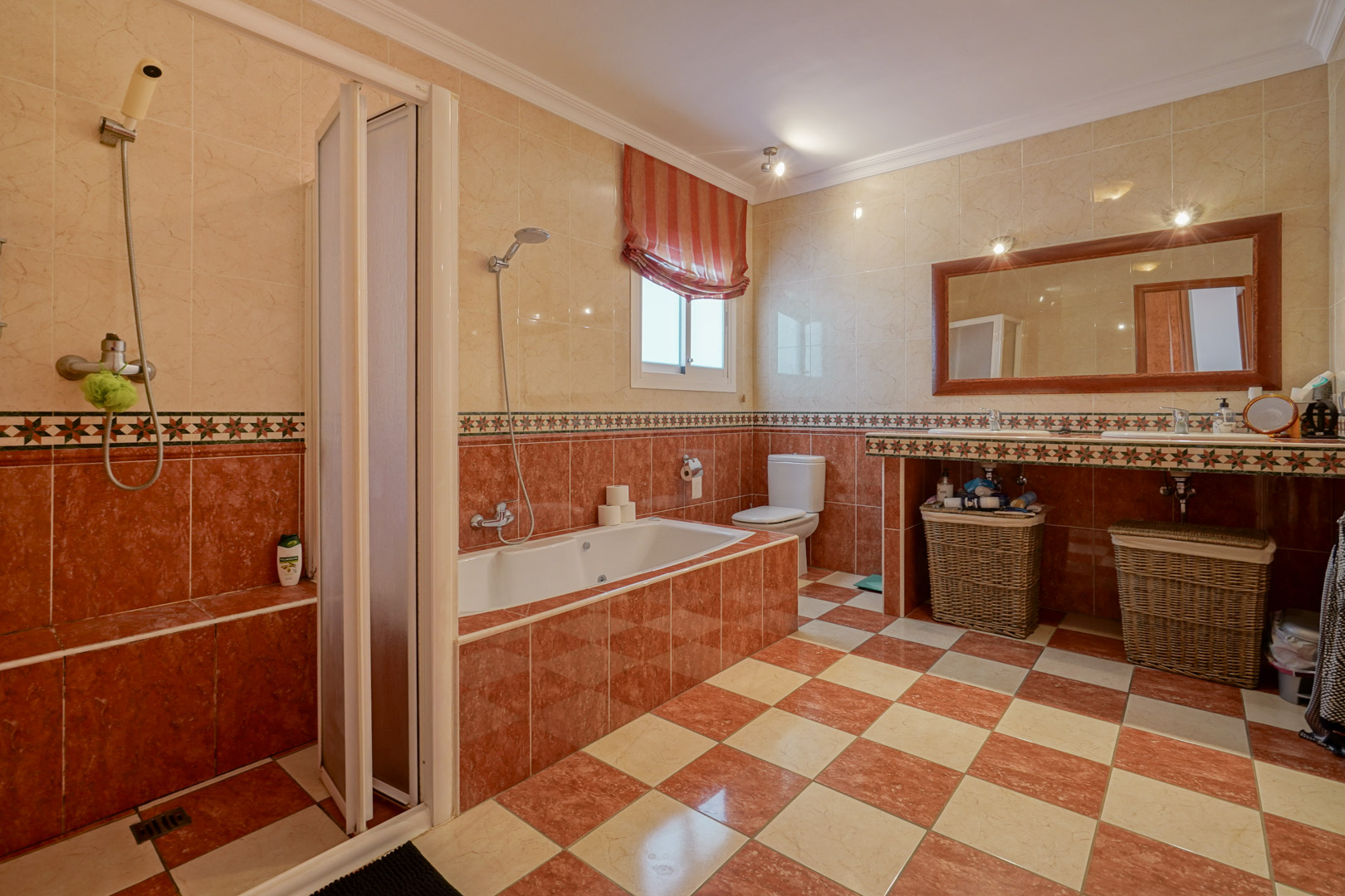 Bathroom featuring cream and reddish marble-effect tiles, a built-in bathtub, separate walk-in shower, and a double vanity with a large wood-framed mirror.