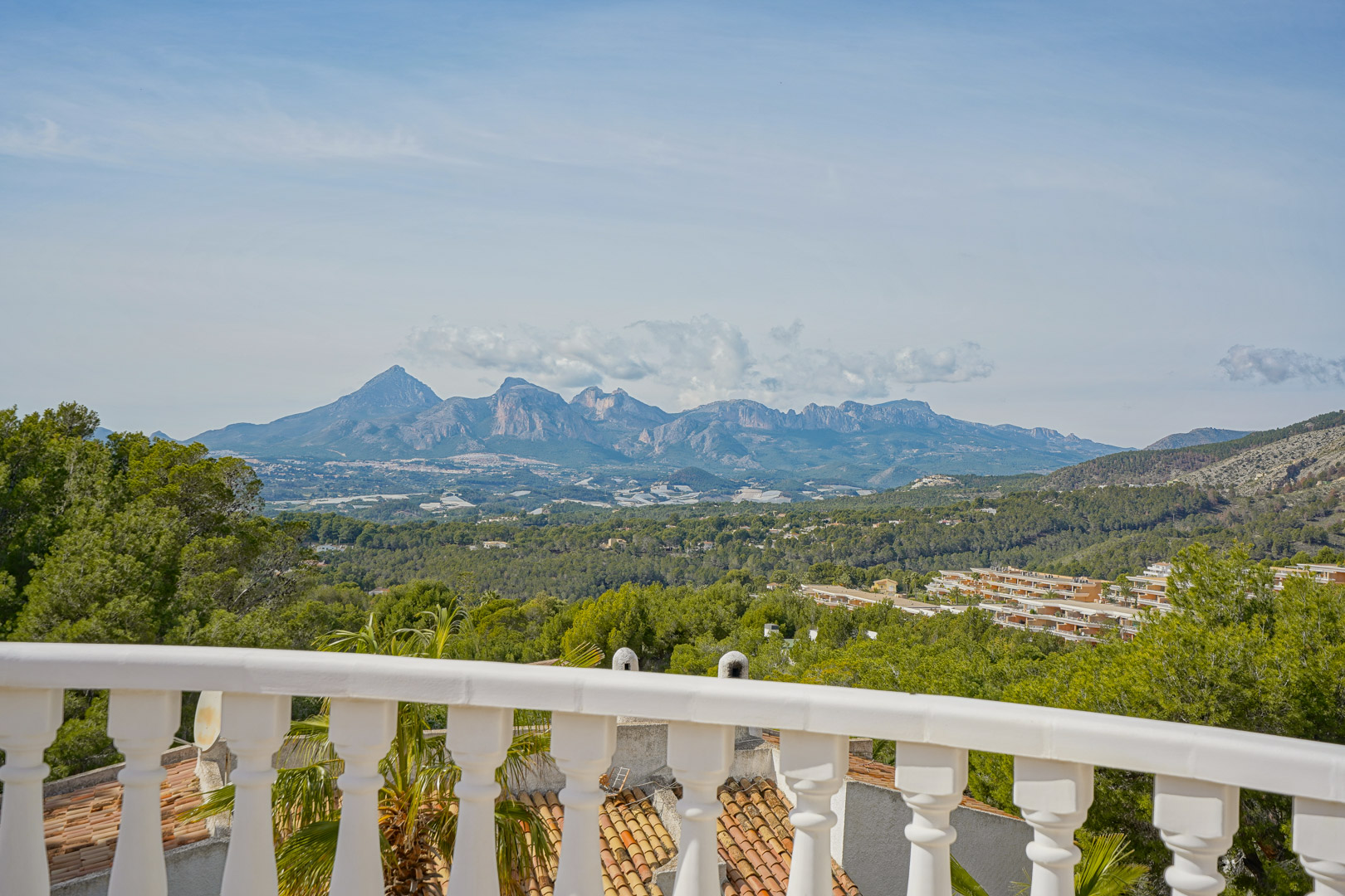 Elevated terrace featuring a white stone balustrade with expansive views of the Puig Campana and Sierra Aitana mountain ranges across the valley.