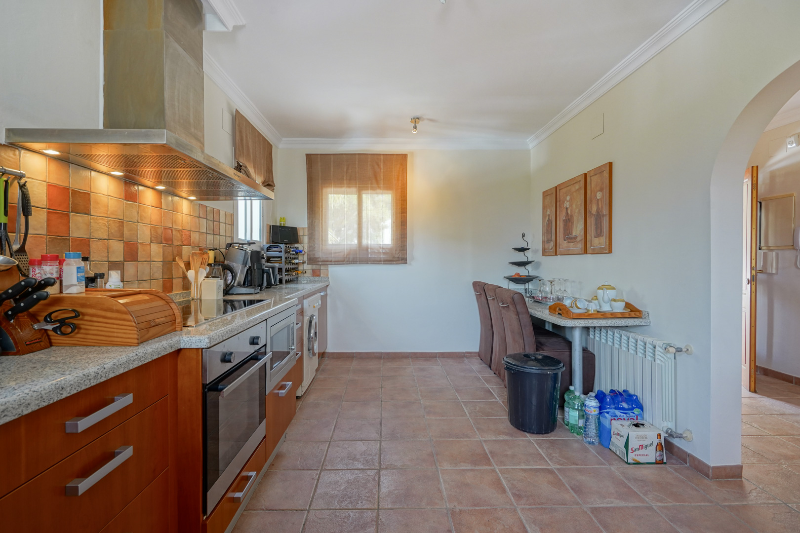 Equipped kitchen featuring wooden cabinetry, granite countertops, and integrated appliances, with terracotta tile flooring and a traditional arched entrance.