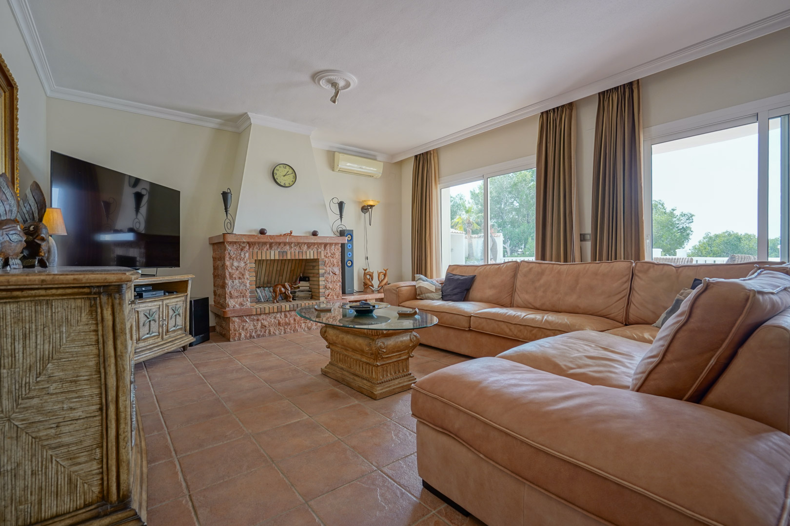 Main living area featuring a rustic stone fireplace, terracotta tile flooring, and a large leather sectional. Sliding glass doors provide natural light and terrace access.