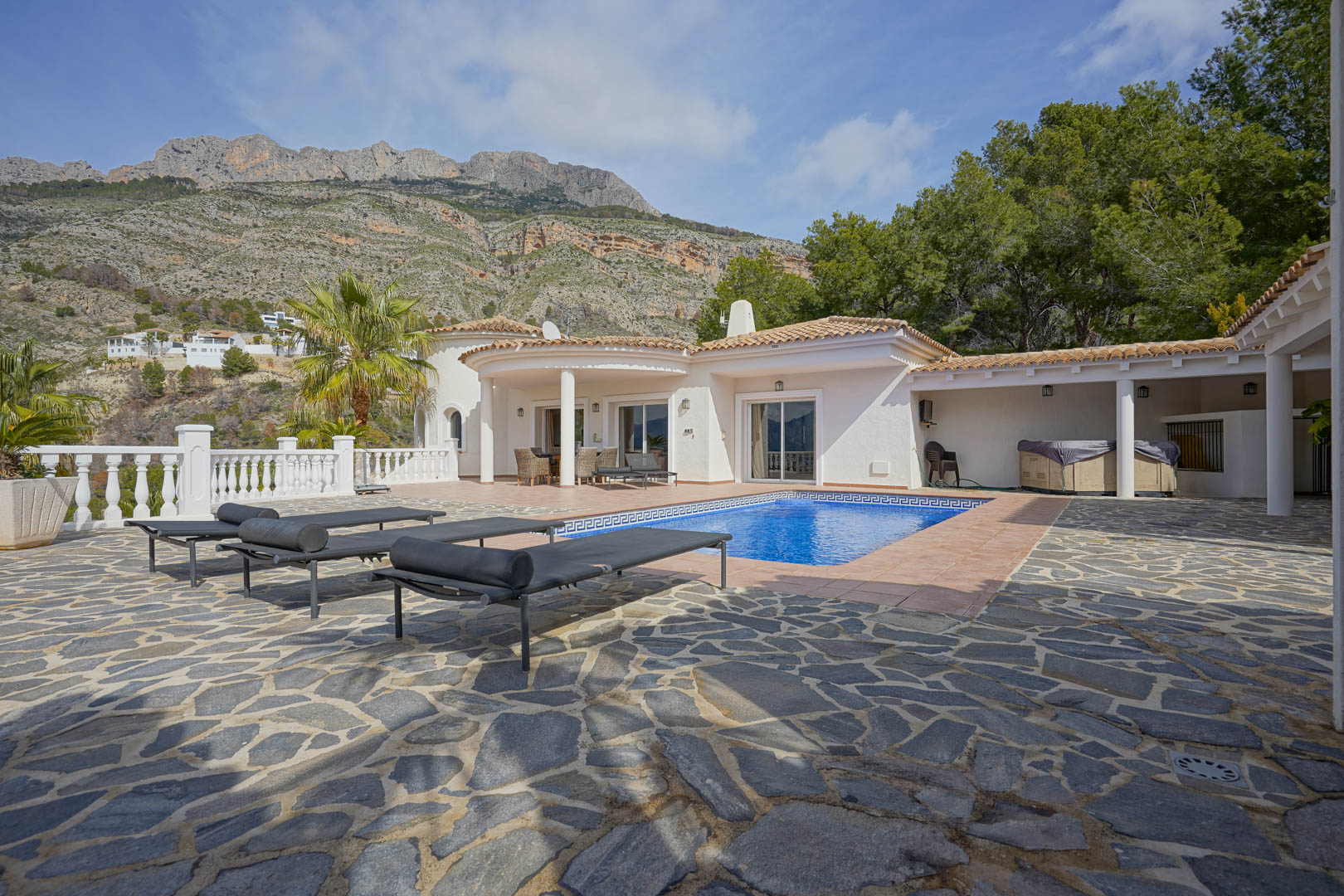 Main terrace with a swimming pool and natural stone paving, featuring direct views of the Sierra de Bernia mountains and the villa's traditional Mediterranean design.