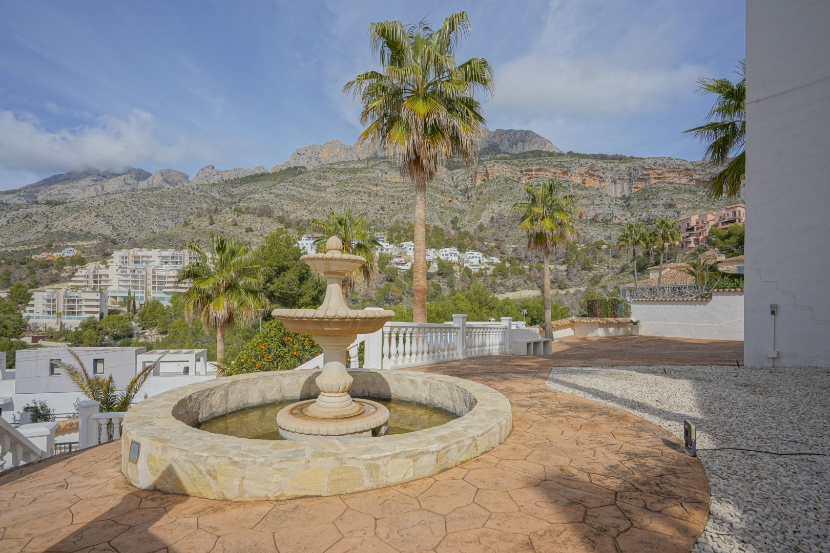 Outdoor terrace featuring a tiered stone fountain and stamped concrete flooring, offering expansive views of the Sierra de Bernia mountain range.
