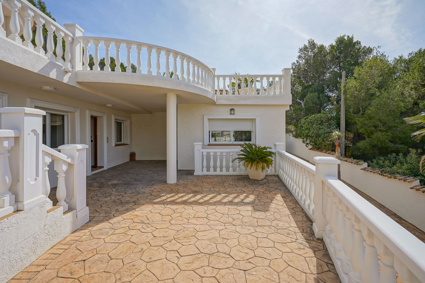 Outdoor terrace featuring stamped concrete flooring and classic white balustrades, located beneath the curved balcony of the upper level.