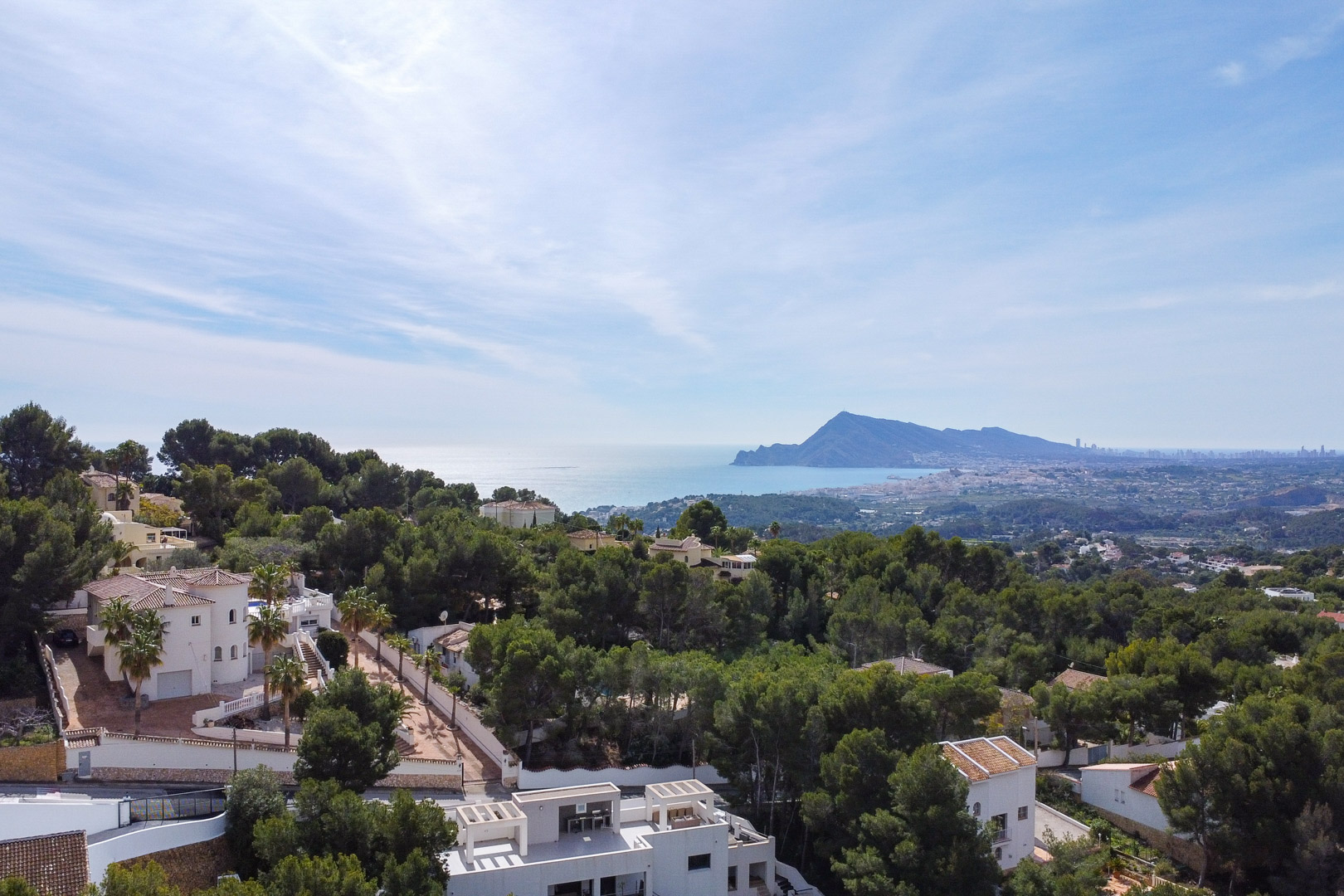 Panoramic aerial view showcasing the lush pine forest, white Mediterranean villas, and the coastline stretching towards the distant Benidorm skyline.