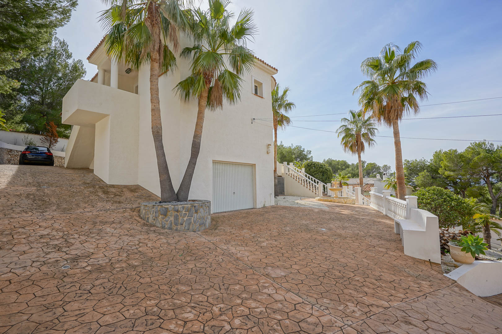 Patterned concrete driveway leading to the integrated garage and main entrance. Tall palm trees and a white facade define the Mediterranean exterior architecture.