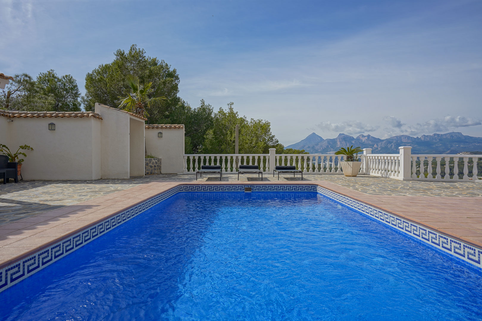 Pool terrace featuring natural stone paving and a white balustrade, overlooking the panoramic mountain peaks of Puig Campana and Sierra Aitana.