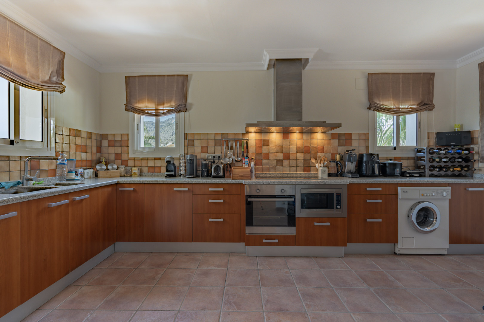 Rustic kitchen featuring wooden cabinetry, granite countertops, and a tiled backsplash. Includes integrated appliances and windows offering views of the surrounding mountains.