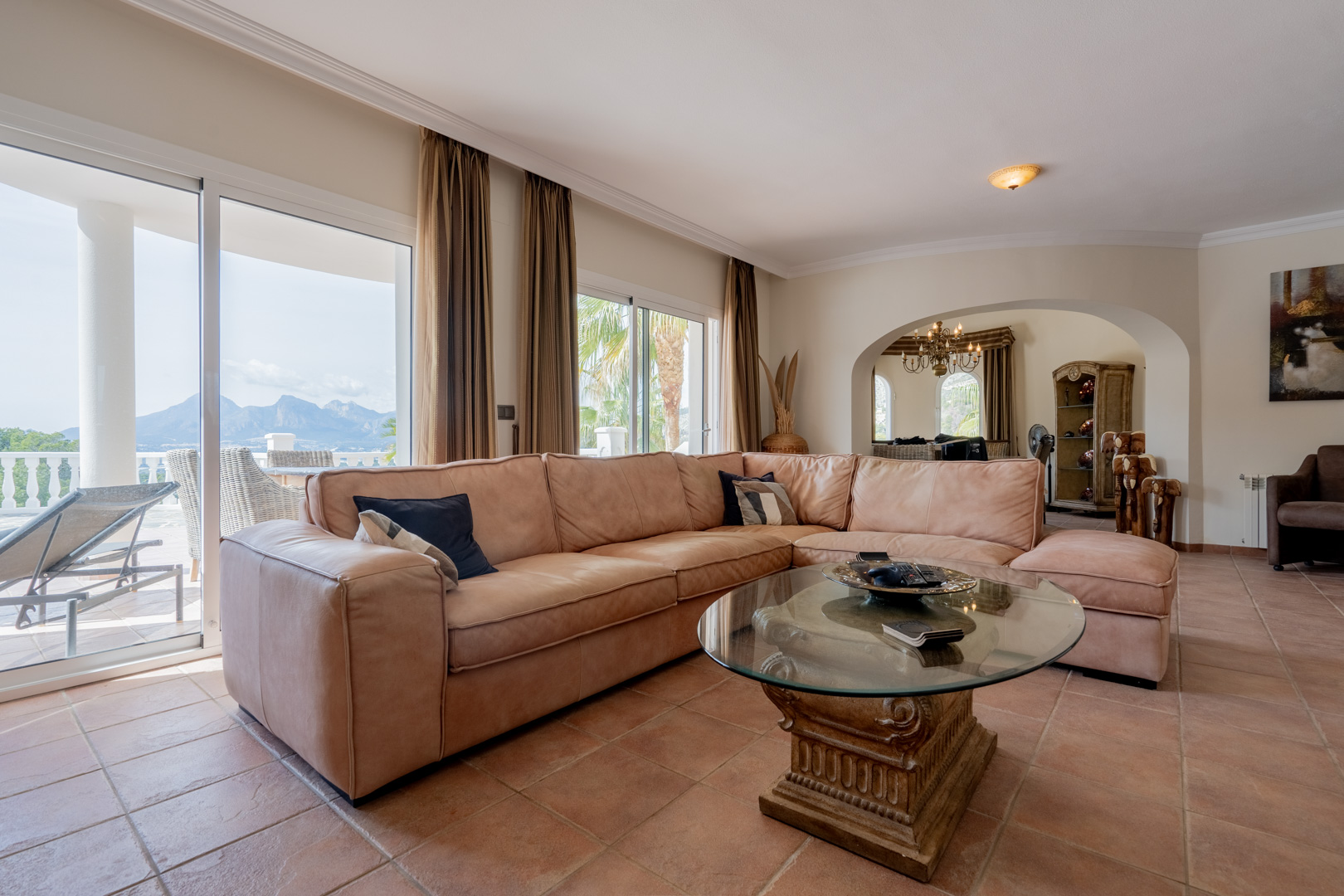 Spacious living area featuring terracotta tile flooring, a leather sectional sofa, and sliding glass doors opening to mountain views and the pool terrace.