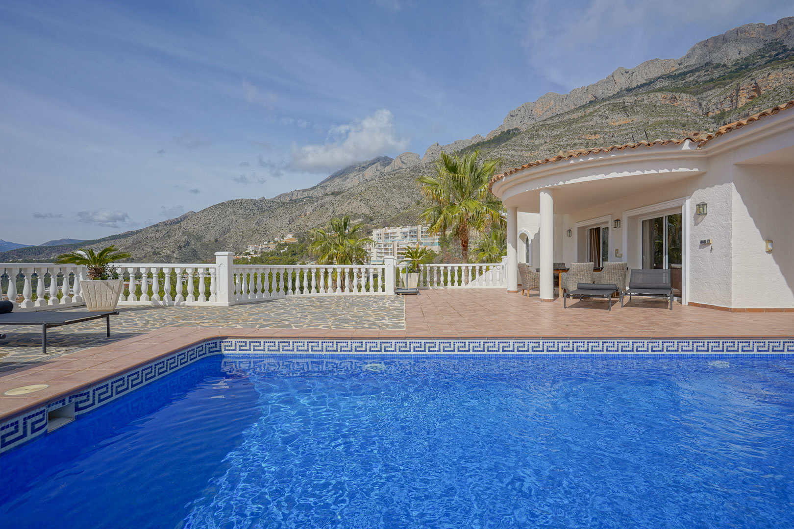 Terrace featuring a blue-tiled swimming pool and covered porch, with panoramic views of the Sierra de Bernia mountains and Mediterranean landscape.