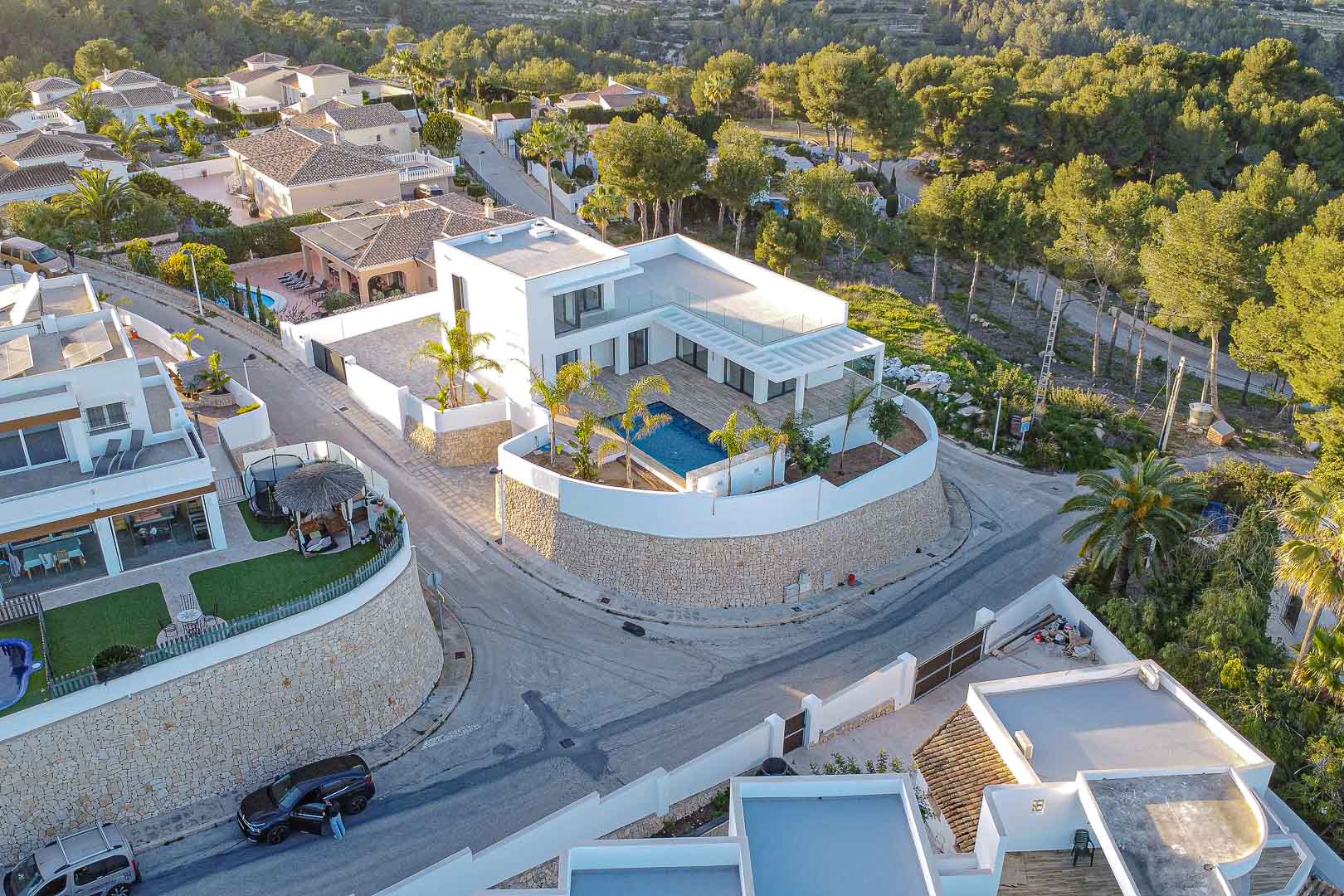 Aerial view of modern villa with blue pool, surrounded by stone wall and greenery in Benimeit, Moraira.