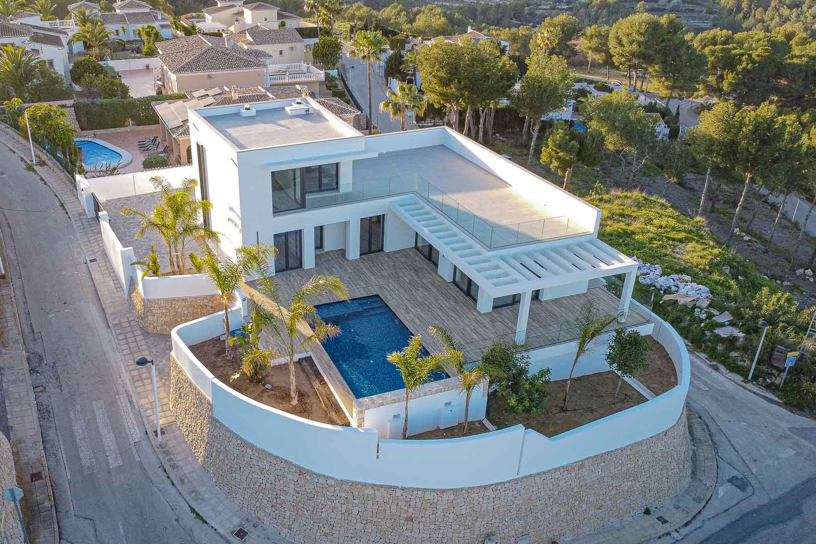 Aerial view of modern villa with blue pool, wooden terrace, and Mediterranean garden in Benimeit, Moraira.