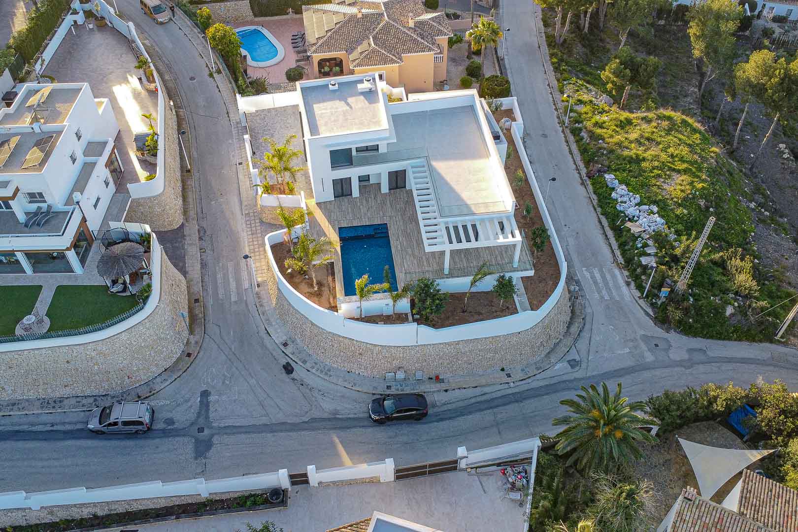 Aerial view of modern villa with blue pool, wooden terraces and Mediterranean garden in Benimeit, Moraira.