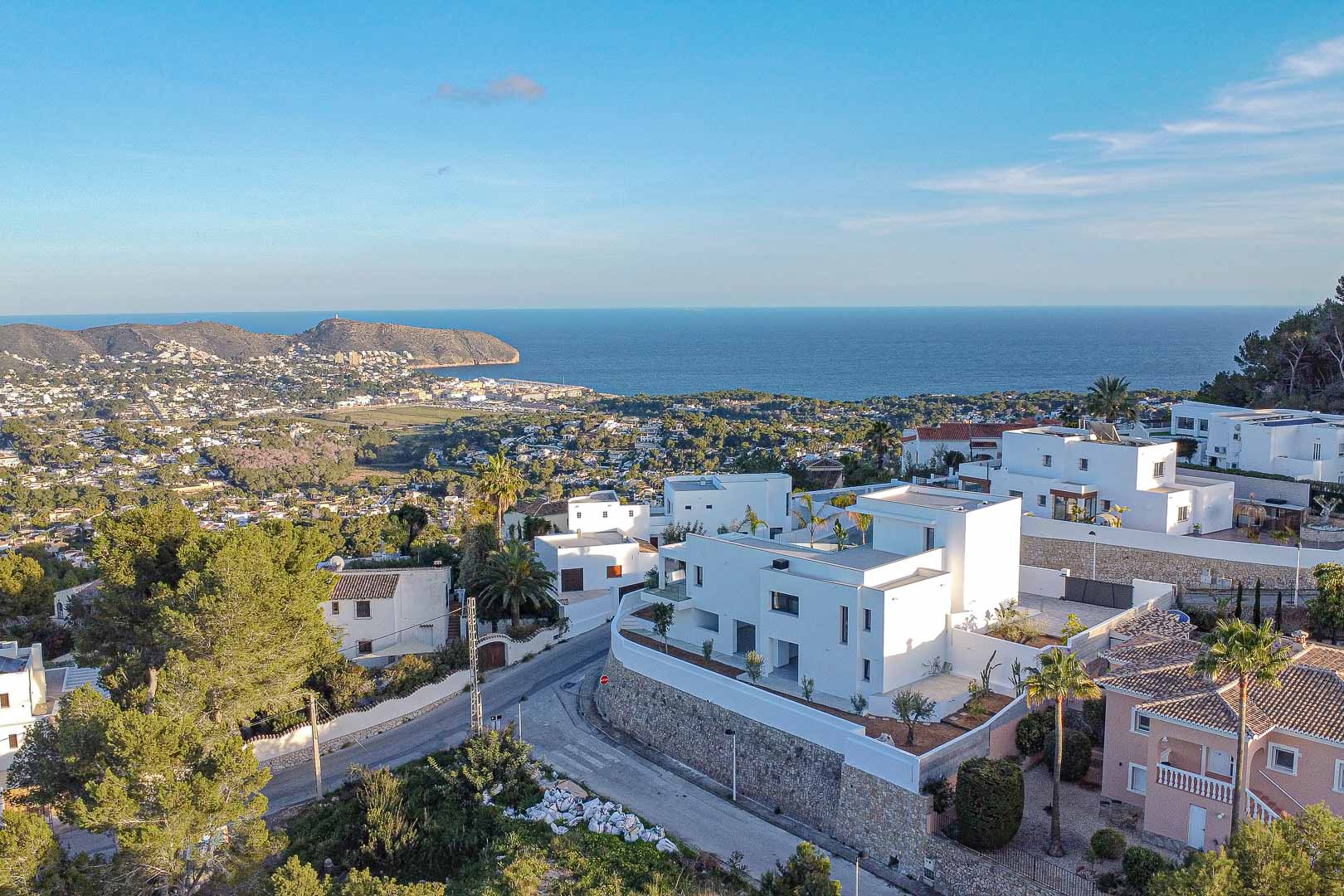 Aerial view of modern white villa in Benimeit with panoramic views of the sea and cityscape.