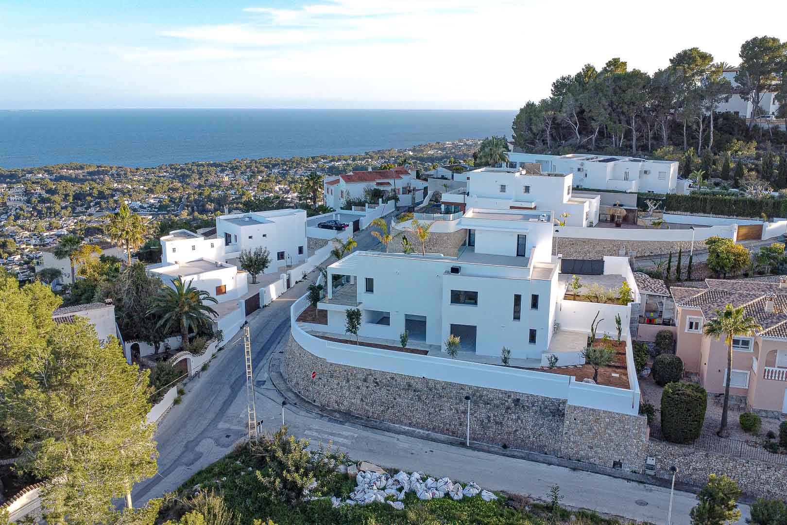 Aerial view of modern white villa with stone retaining walls and sea views in Benimeit, Moraira.