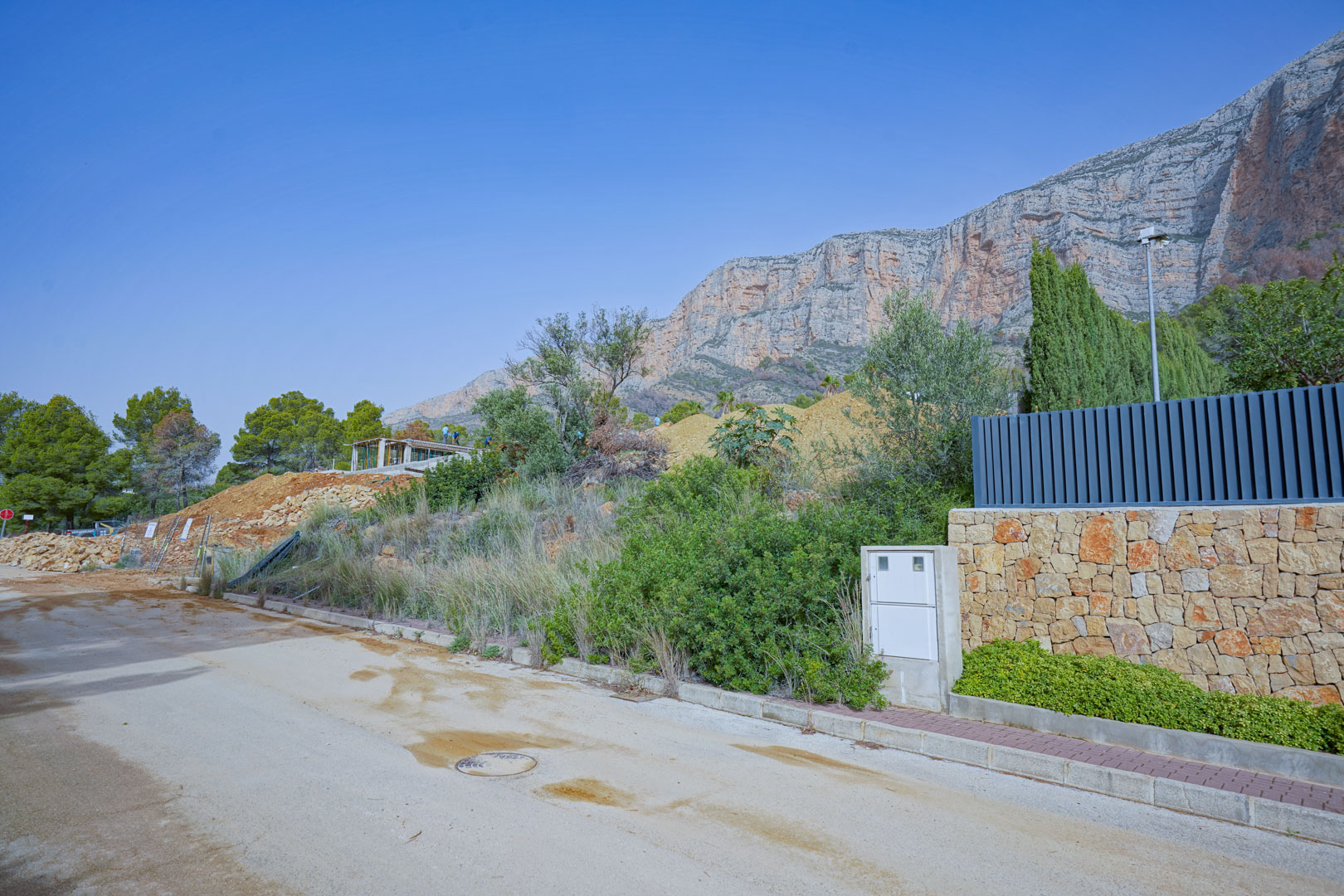 Construction site showing the initial structural phase set against the limestone cliffs of the Montgó mountain with street-level access.