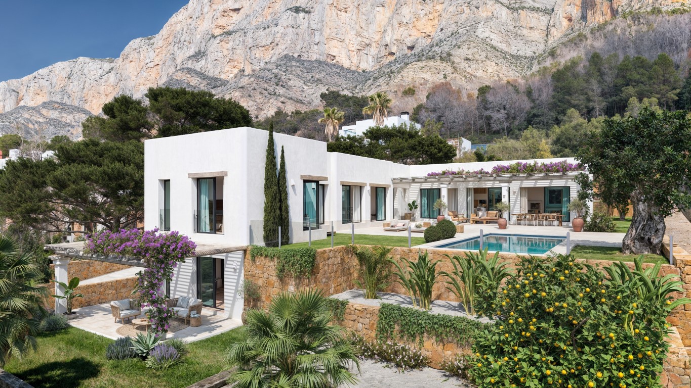 Exterior view of the villa featuring white facades, a private pool, and natural stone walls, set against the dramatic backdrop of the Montgó mountain.