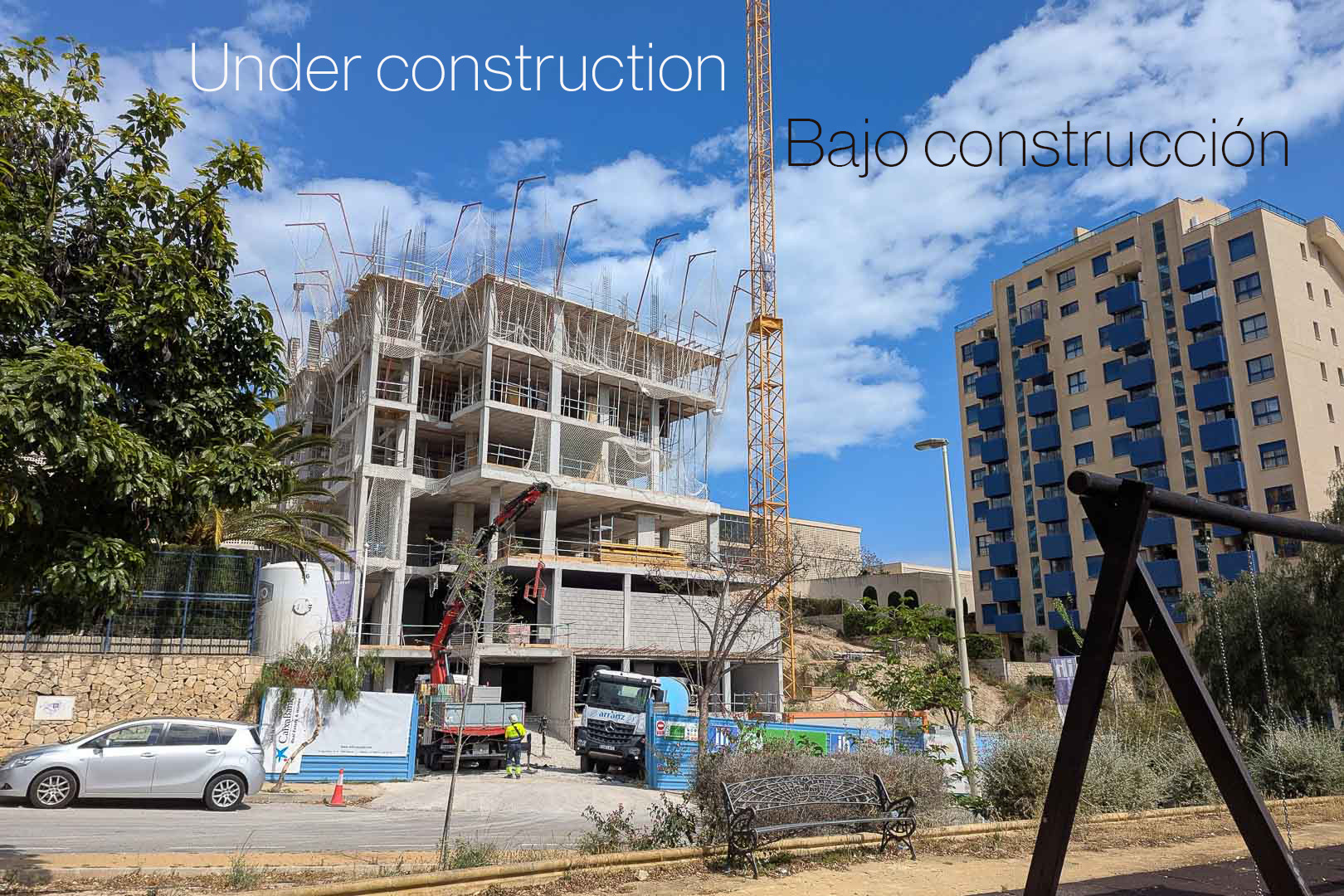 Exterior view of the initial construction phase in Calpe, showcasing the concrete framework, tower crane, and heavy machinery on the residential site.