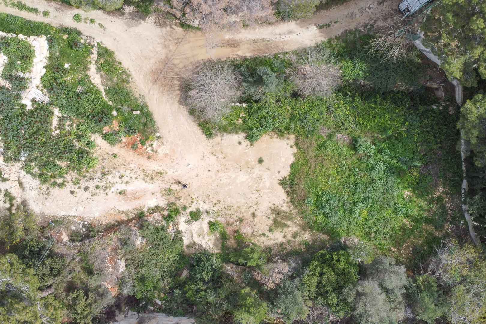 Top-down aerial view of the undeveloped plot, featuring natural Mediterranean vegetation and the cleared site prepared for the custom villa construction.