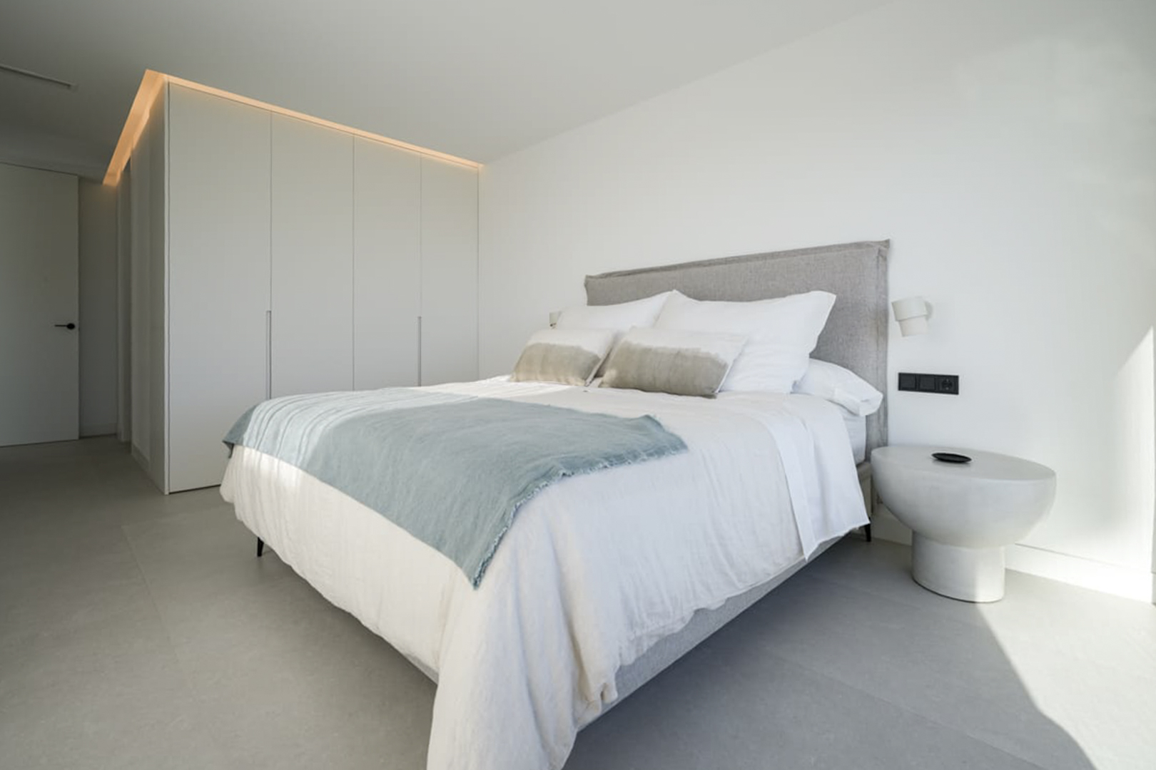 Bright bedroom featuring a double bed, white linens, and a built-in wardrobe with overhead lighting.