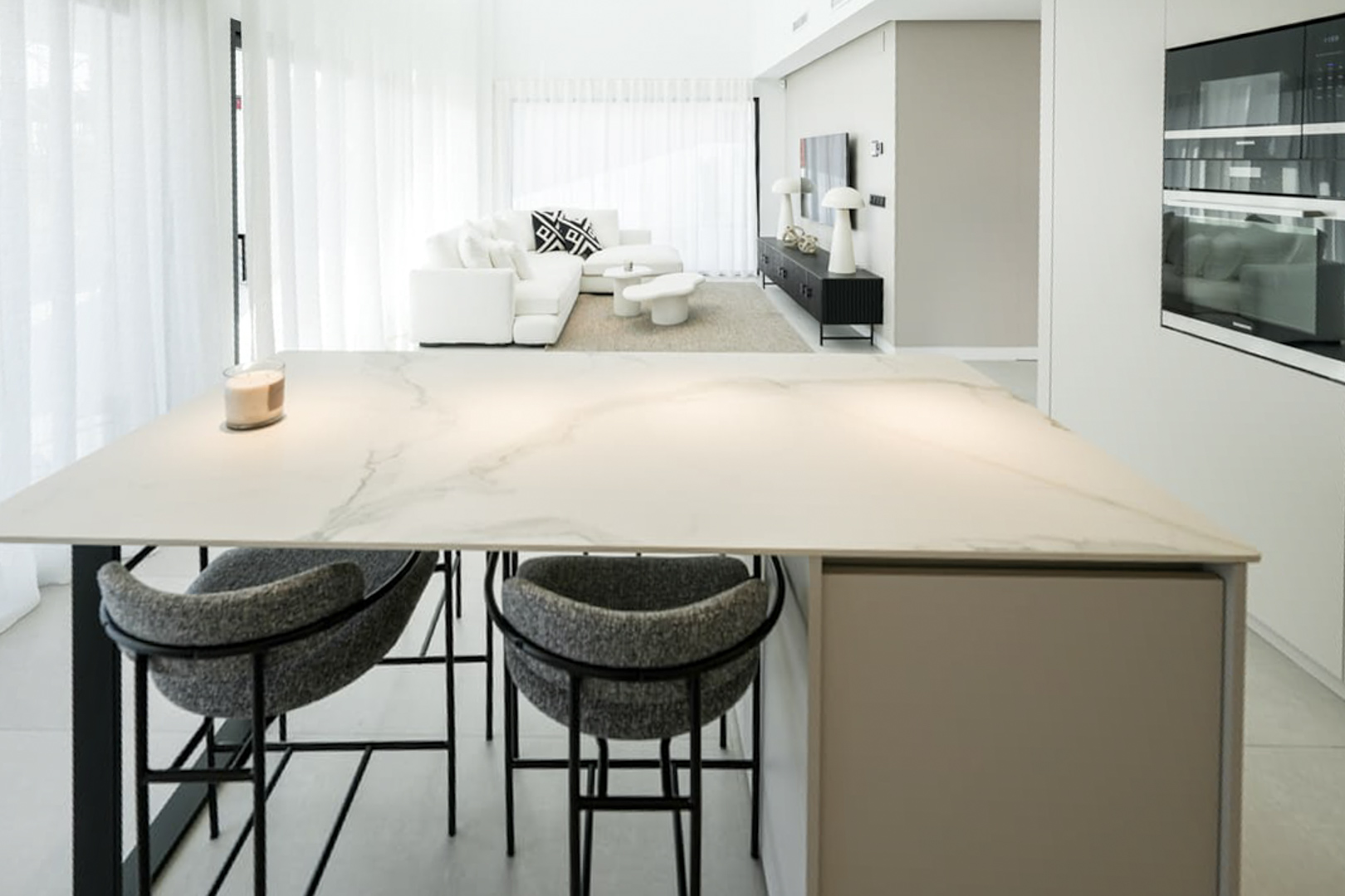 Close-up of the kitchen island with marble countertop and gray upholstered stools.