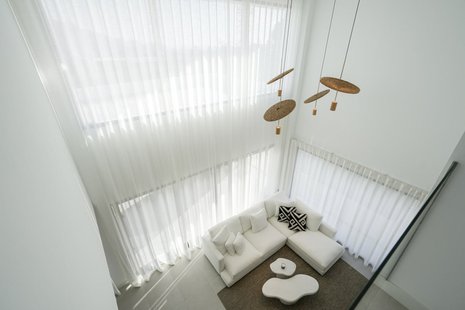 Elevated view of the living room featuring white curtains, a sectional sofa, and designer pendant lights.