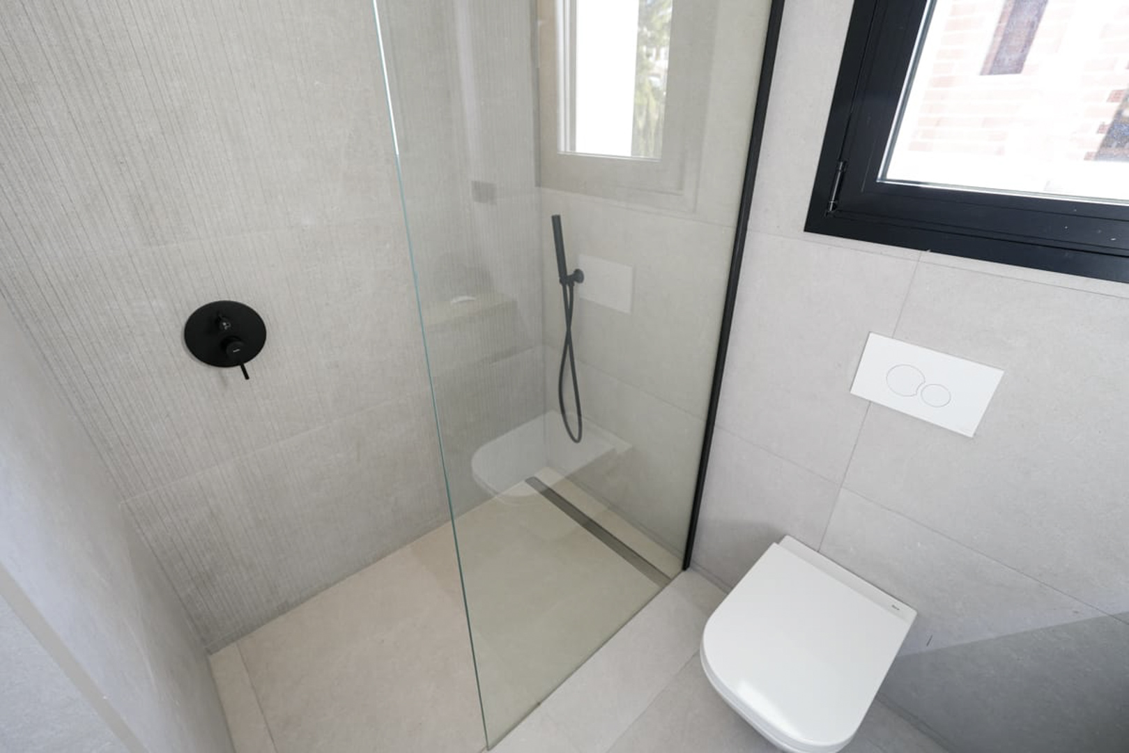Modern bathroom detail featuring a glass shower, black fixtures, and textured gray tiling.