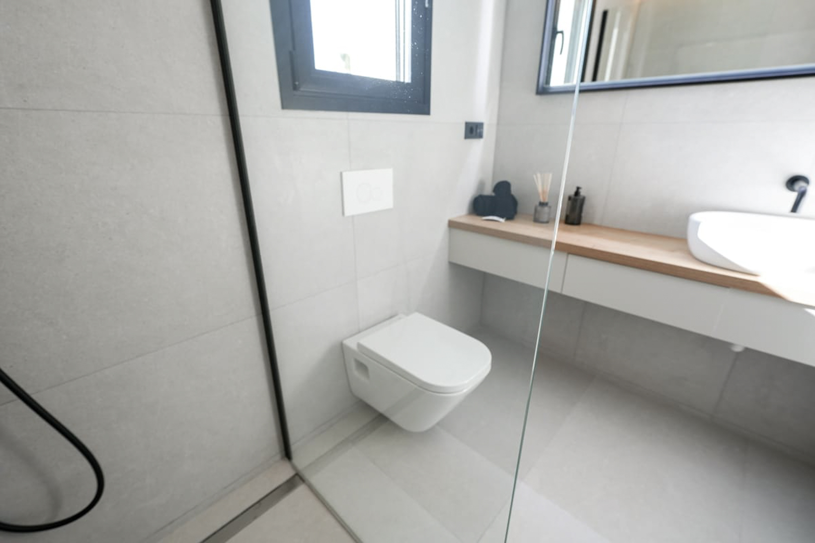 Modern bathroom detail with gray tiles, a wall-hung toilet, and a light wood countertop.
