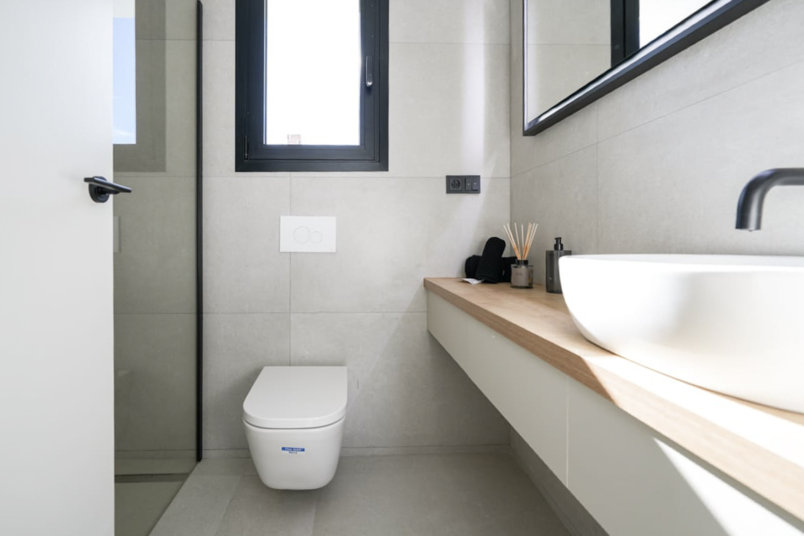 Modern bathroom detail with light wood countertop, white sink, and neutral gray tiling.