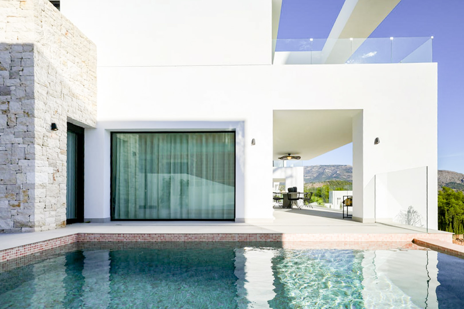 Pool view featuring mosaic tile trim, a stone facade, and a covered terrace with outdoor dining.