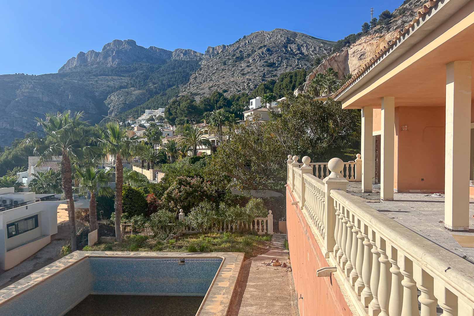 Terrace with a classic stone balustrade overlooking the Sierra de Bernia mountains. The exterior includes a private pool and mature Mediterranean vegetation.