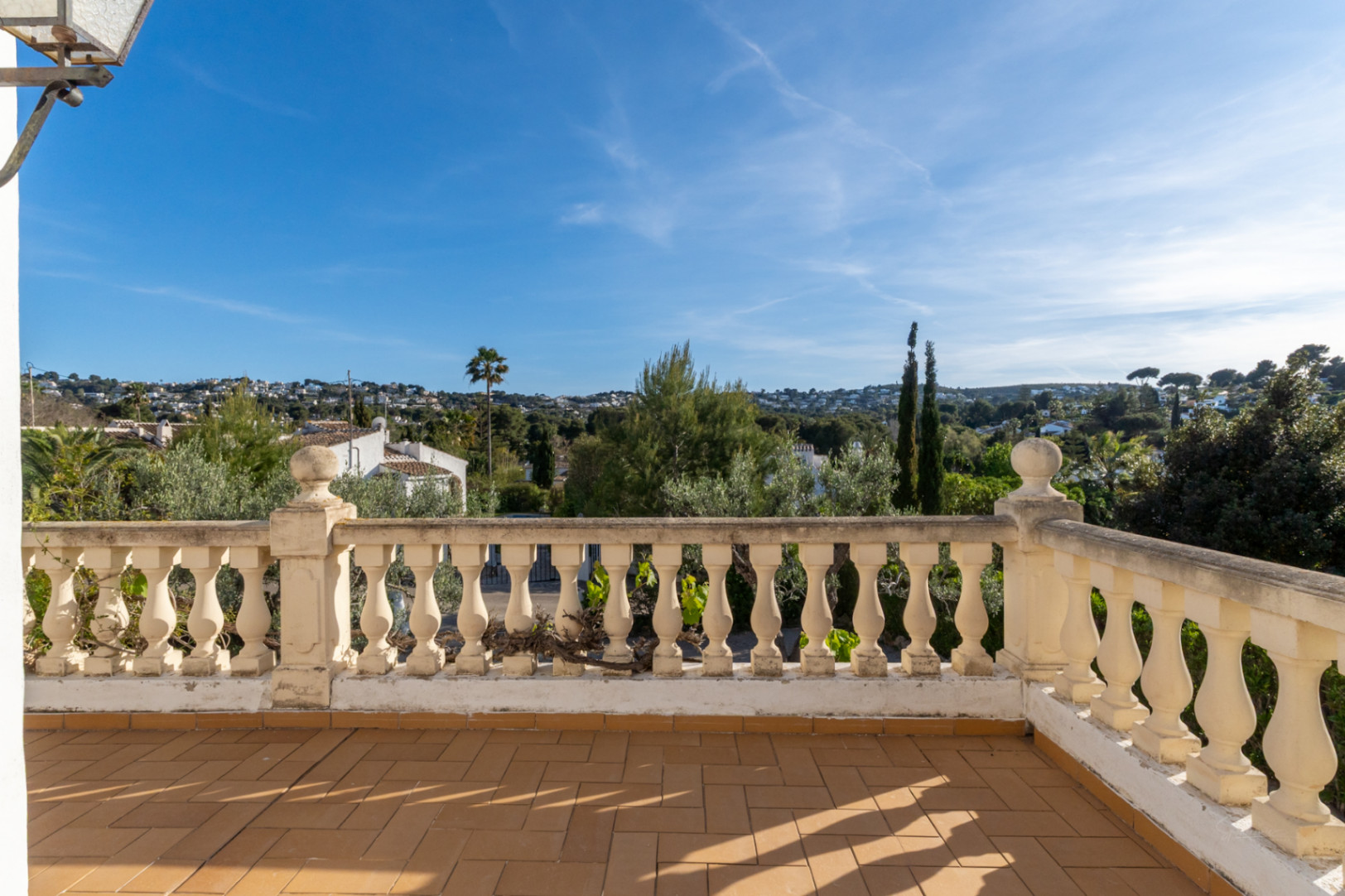 Elevated terrace featuring traditional terracotta tiling and a classic balustrade, overlooking the lush residential landscape of Cap Martí in Jávea.