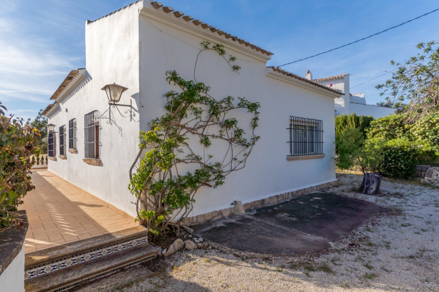 Exterior view of the villa featuring white facades, traditional wrought iron window bars, and a tiled terrace with decorative ceramic accents on the steps.