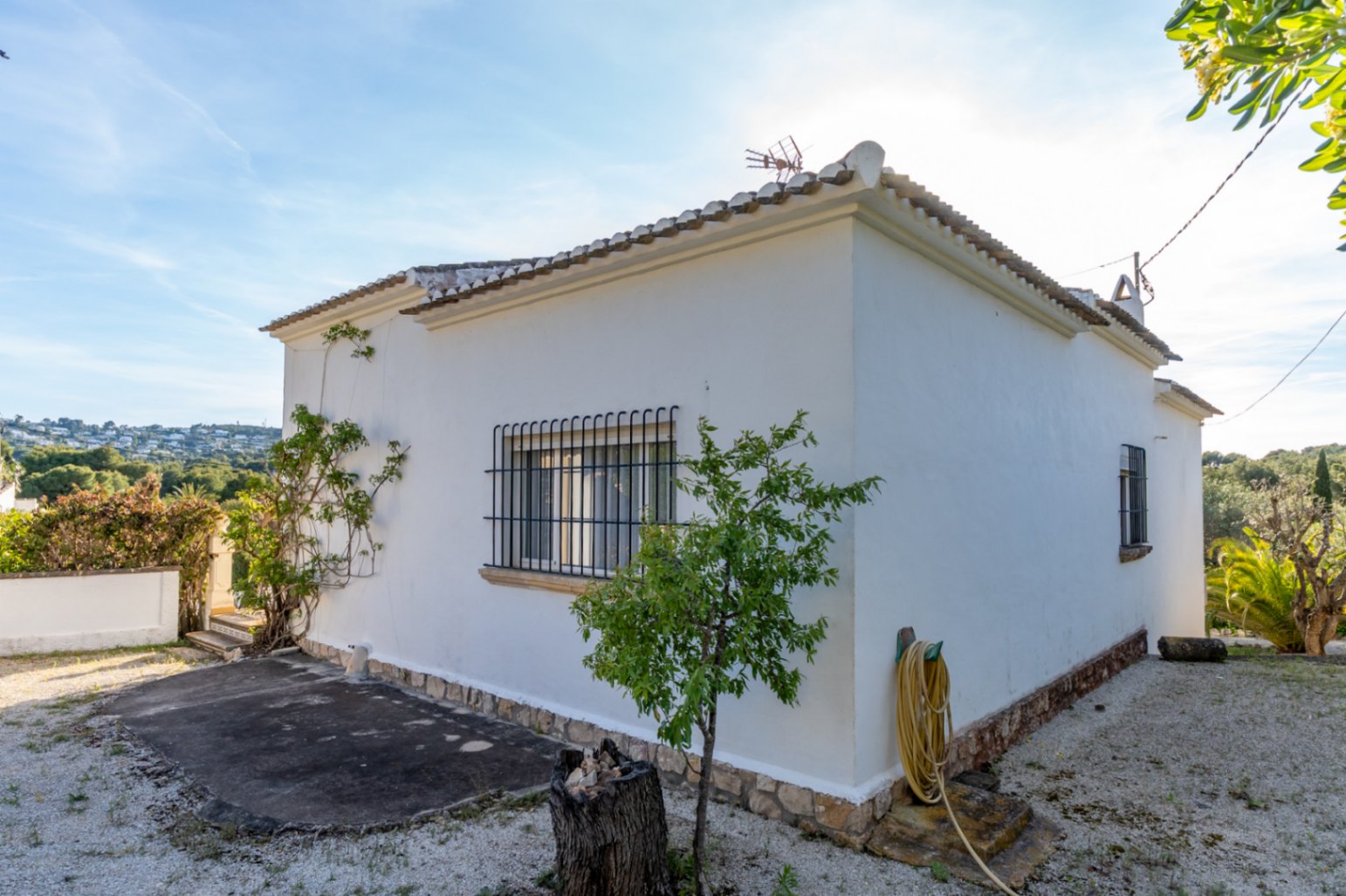 Exterior view of the white villa featuring stone base detailing, traditional tiled roofing, and windows with classic black wrought iron security bars.
